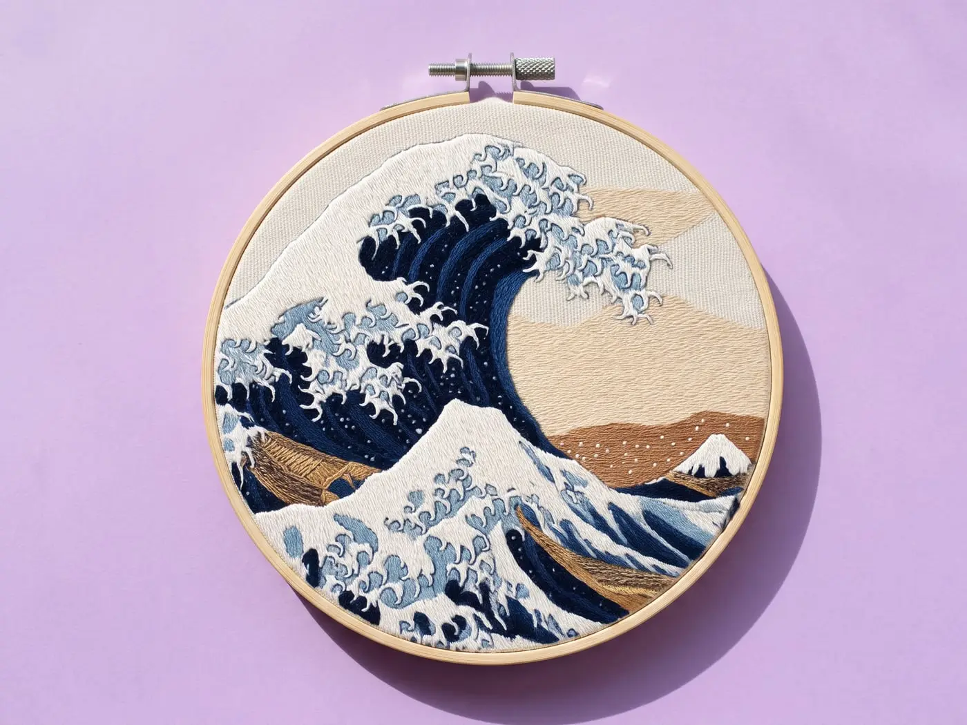 Tambour brodé de la grande vague de Kanagawa en bleus et crème, posé sur un papier lilas